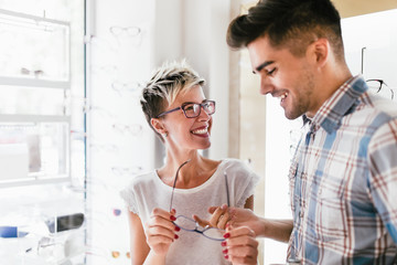 Attractive young couple in optical store buying glasses and smiling