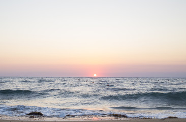 Panorama del sole che tramonta a mare. I colori caldi del tramonto si rispecchiano sull'acqua e le onde del mare agitato.