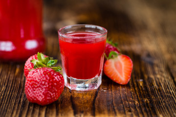 Portion of Strawberry liqueur on wooden background, selective focus