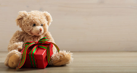 Teddy bear holdimg a gift on a wooden floor