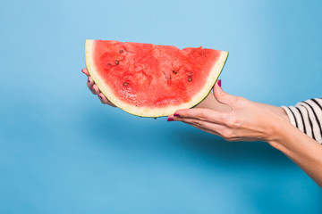 Female hand holding a slice of watermelon on blue background. Summer, holiday, fruit and people concept