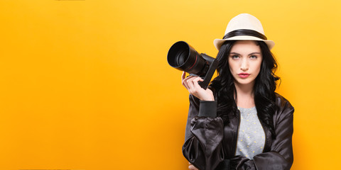  Young woman holding a camera on a yellow background - obrazy, fototapety, plakaty