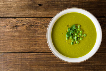 Green pea soup in bowl on wooden table