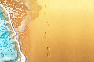 Blue sea wave and footprints on the golden sun-drenched sand of the beach.
