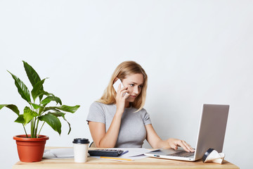Female enterpreneur, being busy with work, keyboarding on laptop computer, calling her business partner while consulting something. Young female freelancer working with modern technologies alone