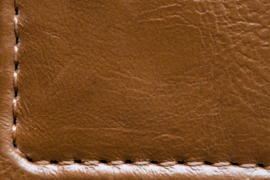 Texture of brown leather with stitches. Element of leather clothing close-up. Seams on leather products