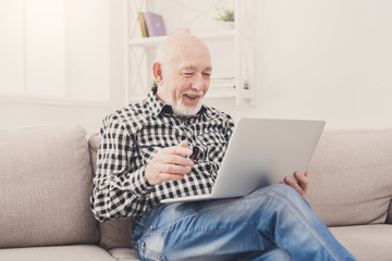 Smiling senior man reading news on laptop