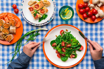 Woman eating healthy food on checkered tablecloth background, top view.