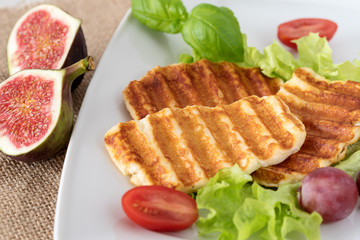Grilled slices of halloumi cheese served on the plate with fig, grapes, lettuce, tomatoes and basil leaf. Halloumi is popular in Cyprus, Greece, and Turkey.
