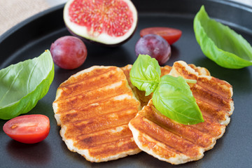 Grilled slices of halloumi cheese served on the plate with fig, grapes, tomatoes and basil leaf. Halloumi is popular in Cyprus, Greece, and Turkey.