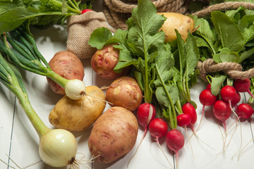 Radishes, potatoes and onions on a white wooden background