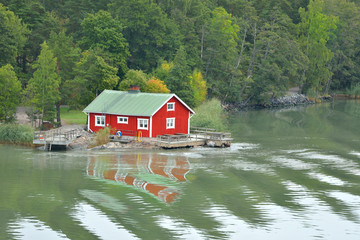 Red wooden traditional Finnish house and pier on bank of island