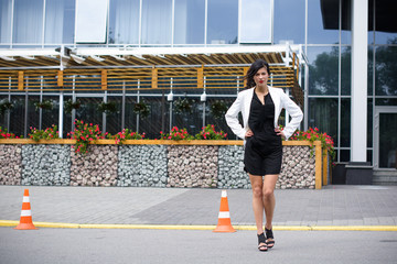 Business woman near the office, a stylishly dressed brunette in a black dress and a white jacket. A lady is waiting for her colleagues near the office