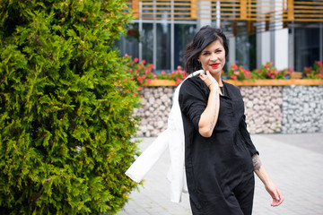 Business woman near the office, a stylishly dressed brunette in a black dress and a white jacket. A lady is waiting for her colleagues near the office