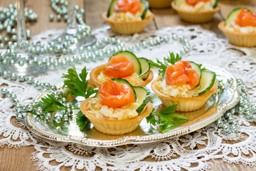 Christmas snack on the festive table. Tartlets with salad, decoration from salmon and cucumber.