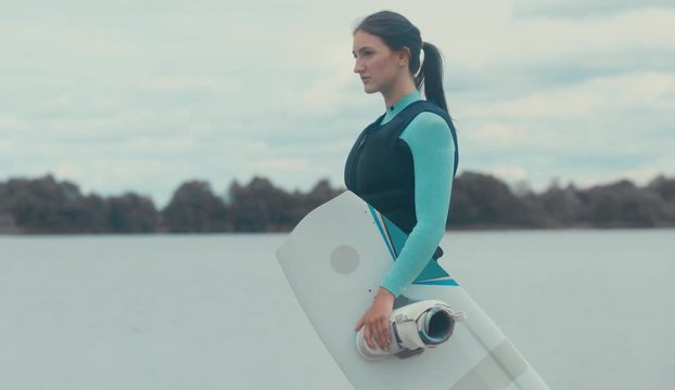 4K CINEMAGRAPH - seamless loop. Attractive female posing in a swimsuit with a wakeboard on a lake, cloudy sky