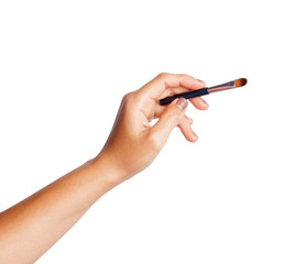 Women's hand with cosmetic accessories: lip pen, eyeshadow brush.
