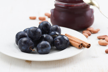 Raw organic plums, jam in jar, raw cocoa beans and cinnamon stick on white background side view