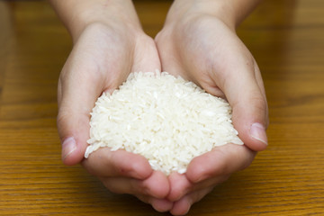 Female hands full of white rice on wooden background