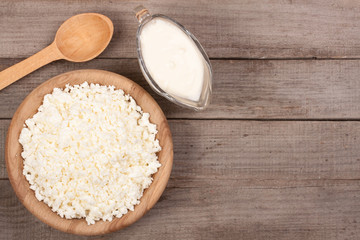 Cottage cheese in a wooden bowl with sour cream on old wooden background with copy space for your text. Top view