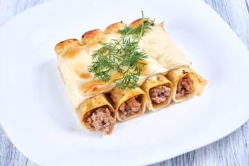 Baked cannelloni with cheese and tomatoes on a white plate