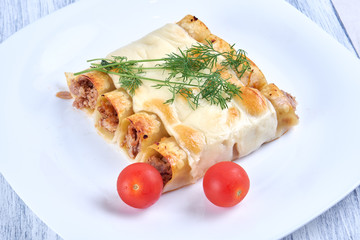 Baked cannelloni with cheese and tomatoes on a white plate