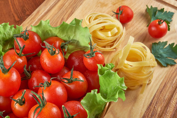 Tomatoes in a wicker basket and green leaves of salad, pasta nests on a wooden Board