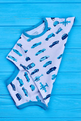 Blue car print cotton bodysuit. New cotton patterned baby boy bodysuit on blue wooden background.