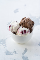 Chocolate and vanilla ice cream with berries on white table in porcelain cup. Space for text