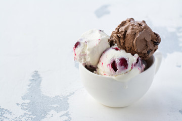 Chocolate and vanilla ice cream with berries on white table in porcelain cup. Space for text