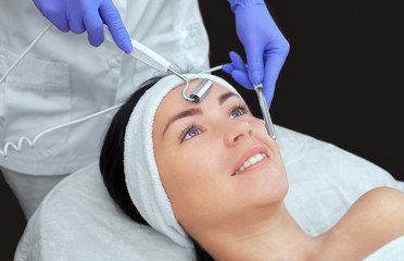The cosmetologist makes the apparatus a procedure of Microcurrent therapy of a beautiful, young woman in a beauty salon. Cosmetology and professional skin care.