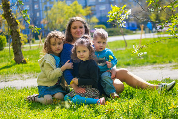 Little girl hugs mother sitting on the grass. Child, playing, threw his mother on grass. Family in spring walks on street.