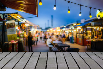 Image of wooden table in front of decorative outdoor string lights bulb in night market with blur...