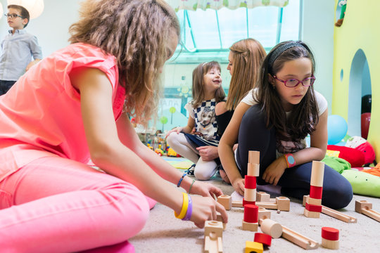 Low-angle view of a cute girl wearing eyeglasses while using wooden toy blocks for building a difficult structure, in balance during playtime at the kindergarten
