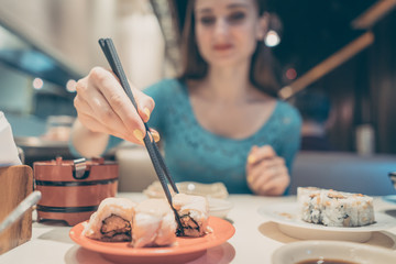 Woman eating sushi food in Japanese restaurant with sticks