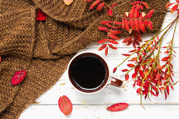 Mug of hot coffee in autumn setting on a wooden table with a knitted scarf, sweater. Comfort, warmth, cozy.