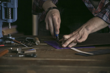 Close up of man hand leather manufacturer performs work on table with tools