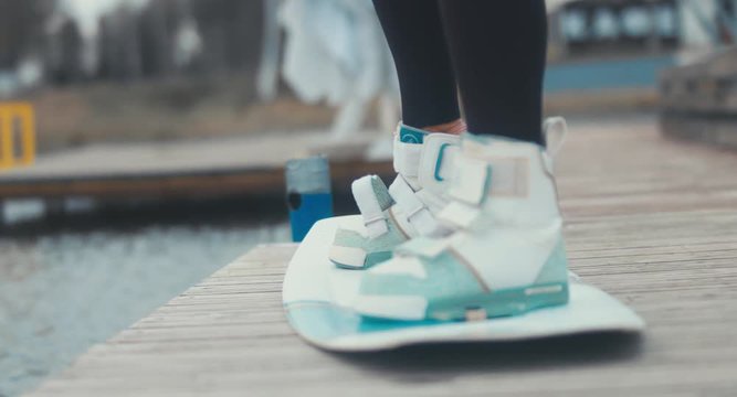 Young female in a swimsuit tightens wakeboard boots, prepares for a wakeboarding session. 4K UHD 60 FPS 