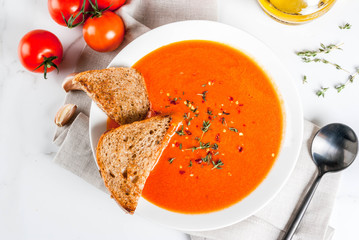 Tomato cream soup with olive oil and herbs, with toasted bread, on white marble background, copy...