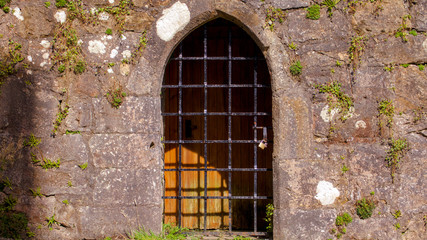 Arched doorway and door with shadow of gate falling upon it in the ruins of Mugdock Castle in Mugdock Country Park near Glasgow in Scotland, UK.