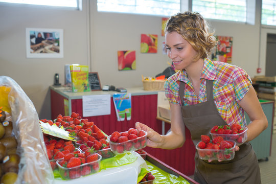 woman tidyin up the strawberry section at a market
