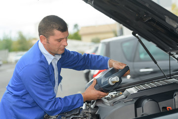 servicing mechanic pouring new oil lubricant into the car engine