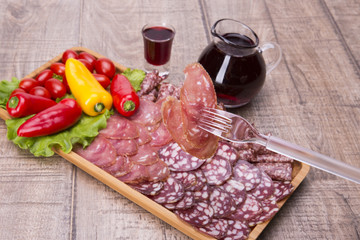 Set of meat delicatessen, tomatoes and peppers, wine on a wooden table.