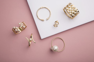 Pearl Golden Bracelets and ring on pink and white background - obrazy, fototapety, plakaty