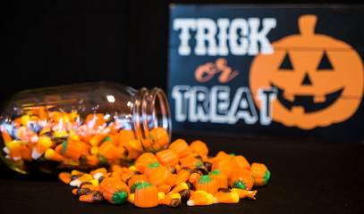 A glass jar has tumbled and spilled all of its candy corn on a table.