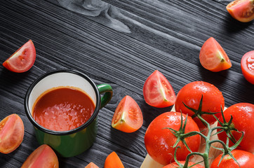 Tomato Juice in Green Enamel Mug on a Black Wooden Table with Fresh Branch of Tomatoes on a Wooden Cutting Board Top View. Background with a Blank Space for Text