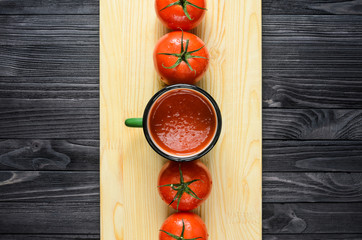 Tomato Juice in Green Enamel Mug on a Wooden Cutting Board on Black Wooden Table with Fresh Tomatoes Top View.