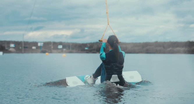 Attractive female wake boarding in a wakepark near a city. 4K UHD 60 FPS 