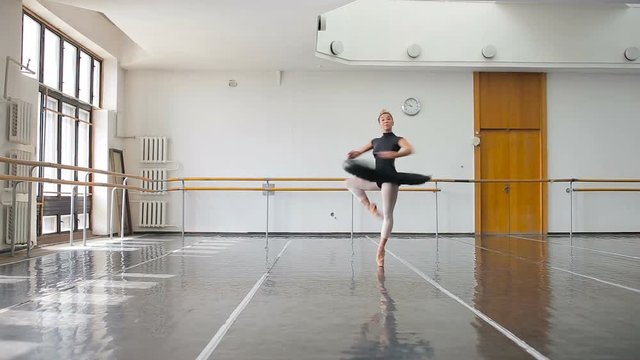 A professional ballerina in a black pack dances in a large training hall