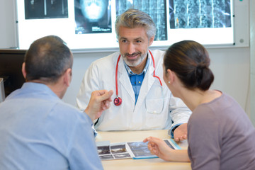 male doctor showing x-ray results to couple in clinic